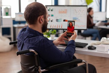 Engelli işadamı elinde akıllı telefon ile uzaktan yöneticisiyle konuşuyor