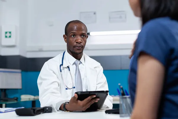 Medico pediatra afroamericano che digita sintomi di malattia sul tablet — Foto Stock