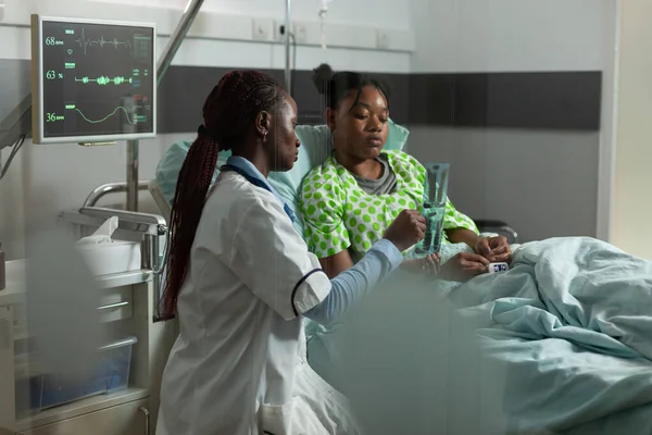 Африканский врач-терапевт, стоящий рядом с больным пациентом во время медицинского осмотра — стоковое фото