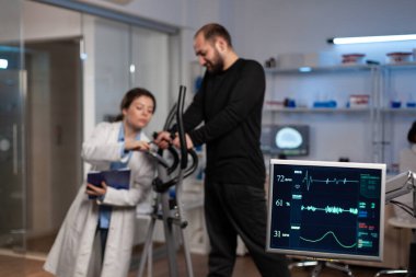 Uzman araştırmacı doktor spor salonundaki eğitim ekipmanlarıyla tartışıyor.