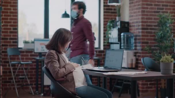 Вагітна працівник з маскою для обличчя використовує ноутбук для роботи — стокове відео