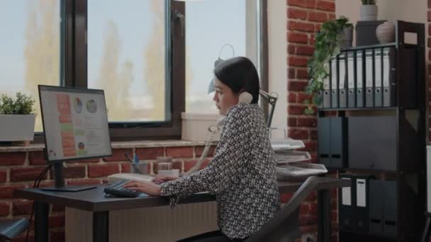 オフィスの電話を使っているアジア人で、コンピュータを使っている。 — ストック動画