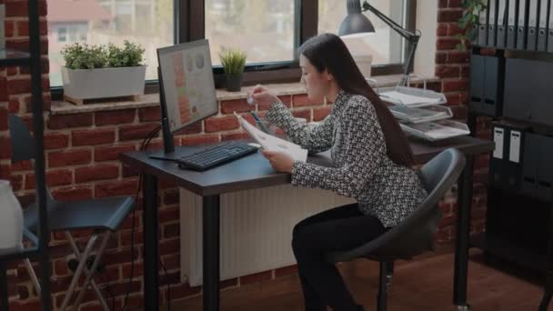 Asiatisk kvinna som jämför diagram på papper och dator — Stockvideo