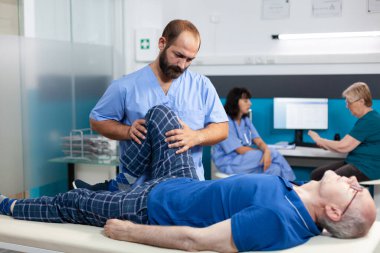 Fizyoterapist yaşlı adamın bacağından yaralanmasına yardım ediyor.