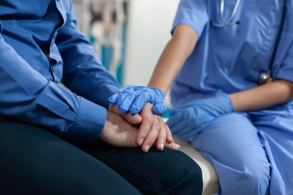 Närbild av sjuksköterska som håller händerna på en gammal patient för stöd — Stockfoto