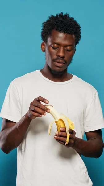 Νεαρός ενήλικας ξεφλουδίζει μπανάνα, ετοιμάζεται να φάει φρούτα για βιταμίνες — Φωτογραφία Αρχείου