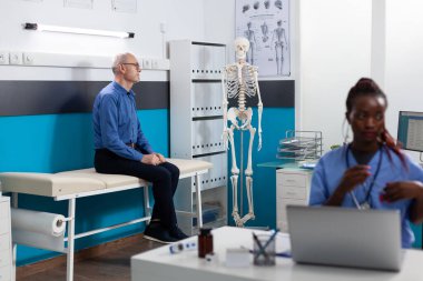 Emekli son sınıf öğrencisi hastane ofisinde yatakta dikiliyor.