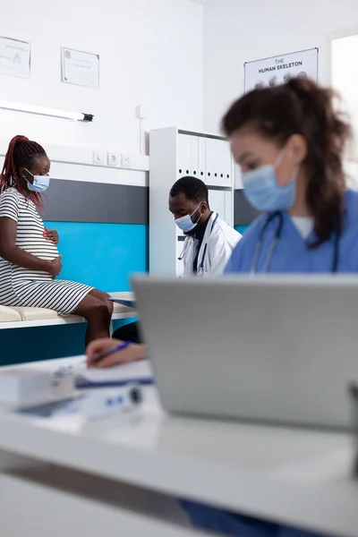 Dokter en patiënt met gezichtsmaskers praten over zwangerschap — Stockfoto