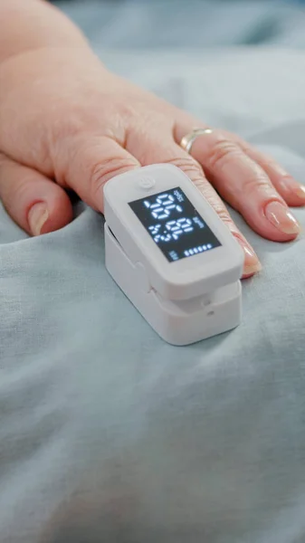 ベッドの中で酸素濃度計を持つ高齢患者の手の閉じる — ストック写真