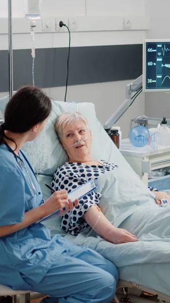 Nurse giving assistance to senior patient with disease in bed — Stock Photo, Image