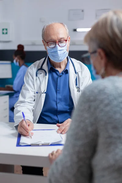 Specialista prendere appunti su appunti mentre fa consultazione con la donna durante la pandemia della congrega 19 — Foto Stock