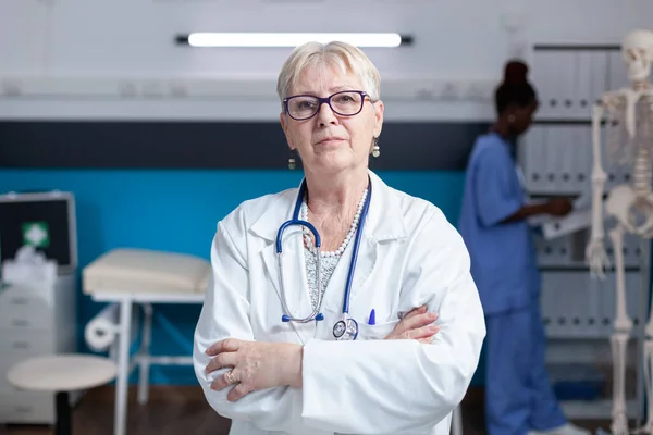 Портрет високопоставленого лікаря, що стоїть з обіймами в кабінеті охорони здоров'я — стокове фото
