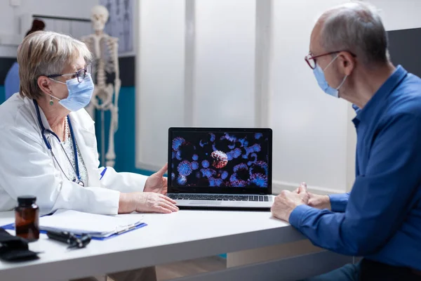 Sjukvårdare talar om covid 19 bakterier på laptop till senior man, bär ansiktsmask — Stockfoto
