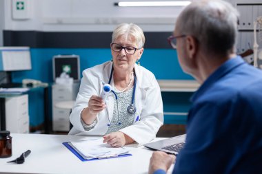 Sıhhiye, eski bir hastanın ateşinin ölçümünü aldıktan sonra termometreye bakıyor.