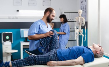 Osteopati uzmanı dizinden yaralanan yaşlı bir hastaya yardım ediyor.