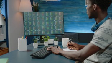 İşadamı borsa veri tablolarını analiz ediyor ve notlar alıyor.