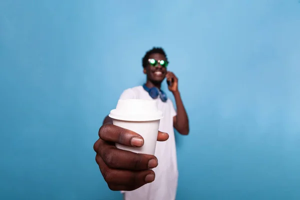 Smiling man with smartphone showing cup of coffee to camera — Stock Photo, Image