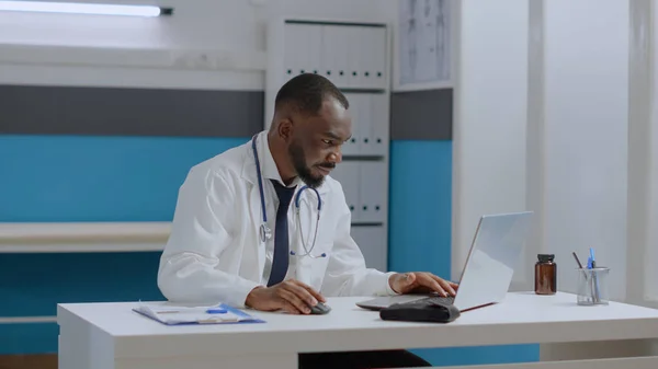 African american therapist doctor sitting at desk in hospital office analyzing sickness diagnostic report — Stock Photo, Image