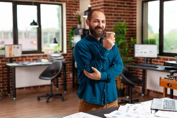 Retrato de un hombre de negocios sonriente sosteniendo una taza de café de pie en la oficina de la compañía startup — Foto de Stock