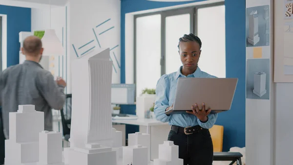 Kvinna ingenjör arbetar på bärbar dator för att planera contruction layout med byggnad modell och maquette — Stockfoto