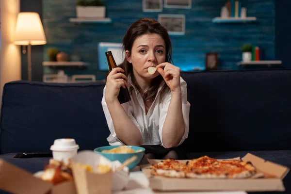 Droevige vrouw die ambachtelijk bier drinkt en chips eet uit de kom aan tafel met grote pizza en afhaaldiner — Stockfoto