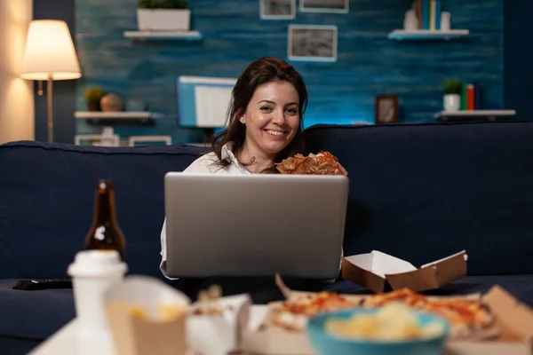 Портрет усміхненої жінки, що дивиться онлайн телевізійний ситком на ноутбуці, що їсть бургер для доставки додому — стокове фото