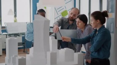 Tablet ve dizüstü bilgisayarla masadaki yapı modelini analiz etmek için çalışan çok ırklı insanlar