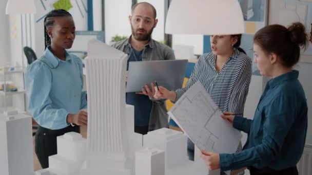 Kollégák, akik laptoppal és tervrajzokkal dolgoznak az irodai épületmodell elemzésén — Stock videók