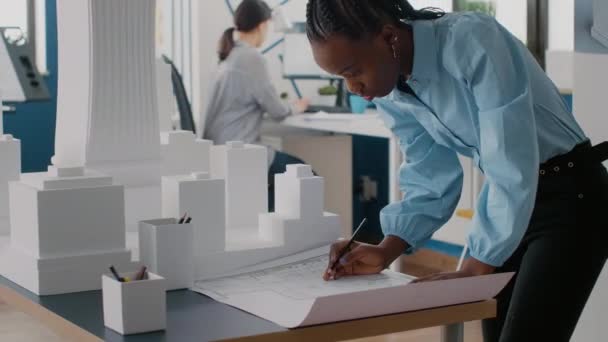 Женщина-инженер рассматривает чертежи планов на столе для проектирования макета строительства — стоковое видео