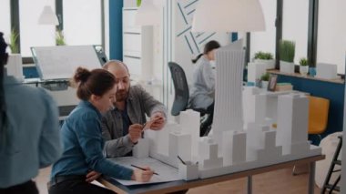 Meslektaşlar, masadaki bina modeli ve planlarını analiz etmek için akıllı telefon kullanırlar.