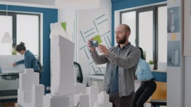 İnşaat planı ve tasarımı için inşaat modeli tasarlamak için cep telefonu kullanan bir adam.