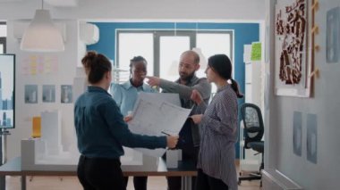 Mimarlardan oluşan çok ırklı bir grup masanın üzerinde planlar ve modellerle çalışıyor.