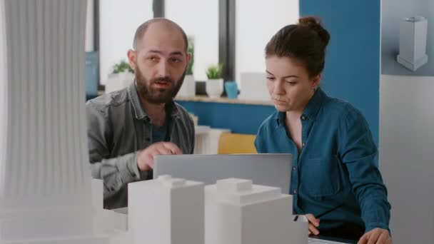 Рабочие проектируют модель здания и макет на ноутбуке в архитектурном офисе — стоковое видео