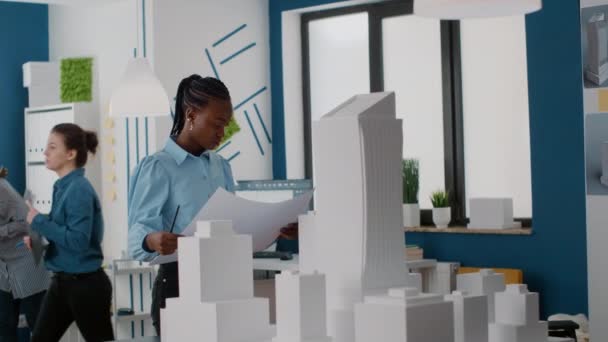 Žena stavitel analyzuje plány na návrh dispozice staveniště a model budovy — Stock video