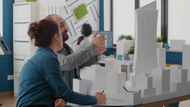 Архитекторы, использующие смартфон для проектирования макета здания с моделью здания и чертежами — стоковое видео