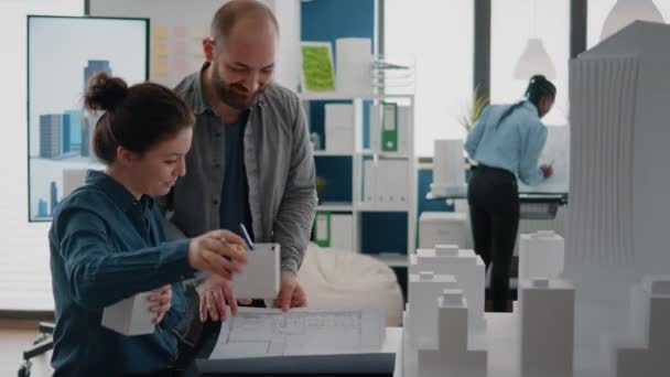 Equipo de compañeros de trabajo analizando el modelo de edificio y el plan de planos en la mesa para diseñar el diseño de la construcción — Vídeos de Stock