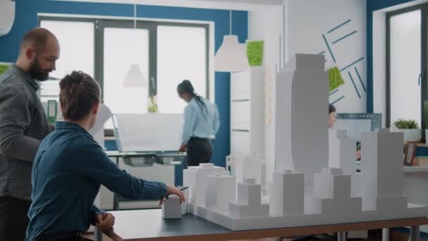 Férfi és nő elemzi a tervrajzokat és az épület modelljét a városépítés megtervezéséhez — Stock videók