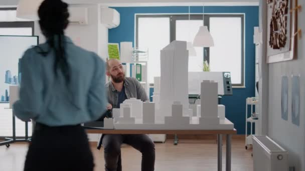 Сотрудники смотрят на планшет и модель здания, чтобы получить вдохновение для городского проекта — стоковое видео