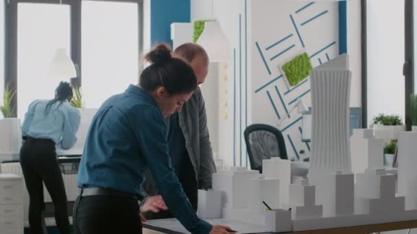 Tým architektů plánuje návrh s plány a model budovy na stole — Stock video