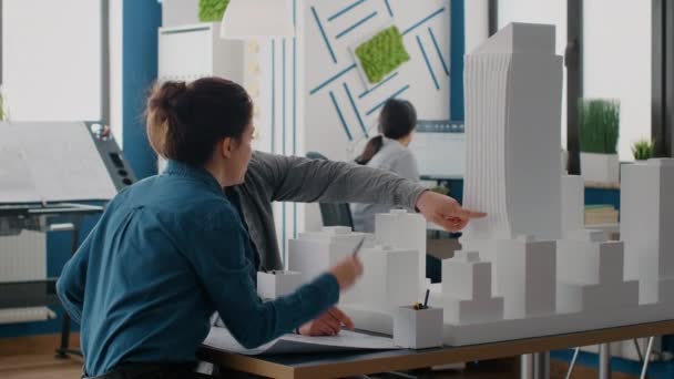 Коллеги выполняют командную работу по проектированию макета здания с использованием модели здания и чертежей — стоковое видео