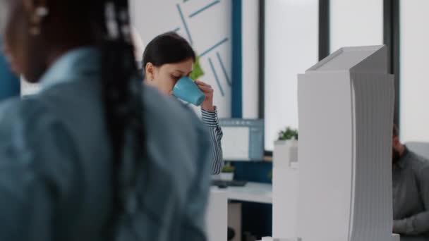 Портрет женщины-инженера, смотрящей на модель здания и пьющей чашку кофе на работе — стоковое видео