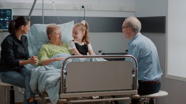 Çocuk, hastane koğuşundaki aile ziyaretinde hasta büyükanneye sarılıyor.