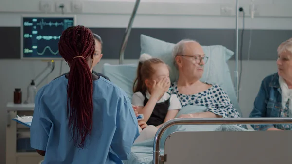Nahaufnahme einer Krankenschwester, die einem alten Mann und seiner Familie bei einem Besuch die Diagnose erklärt — Stockfoto