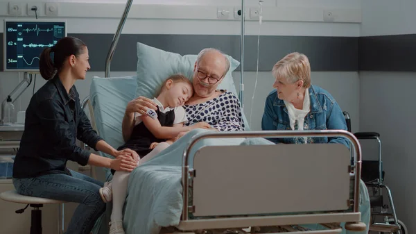 Nichtje knuffelen ziek opa op bezoek in ziekenhuis afdeling bed — Stockfoto