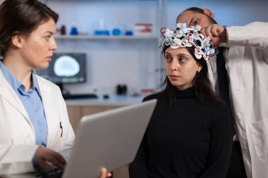 Nörolog elinde dizüstü bilgisayarla kadın hastaya tomografi gösteriyor.