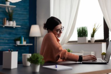 Uzaktan kumandayla çalışan gülümseyen bir öğrenci bilgisayar kullanırken telefonla konuşuyor..