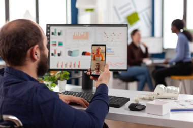 Engelli iş adamı elinde akıllı telefonla uzaktan kumanda ekibiyle konuşuyor.