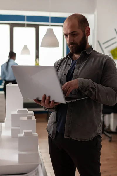 Architekt drží notebook a porovnává plány s maquette mrakodrapu — Stock fotografie