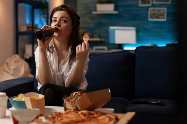 Mujer vestida casual bebiendo cerveza de botella mientras sostiene una patata frita — Foto de Stock