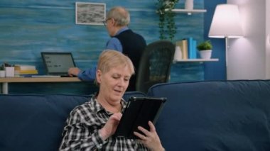 Evdeki kanepede oturmuş dijital tablette e-postaları okuyan son sınıf öğrencisi bir kadın.